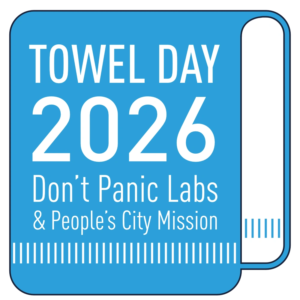 towel-day-2026 | Don't Panic Labs Blue towel-shaped graphic reading “Towel Day 2026” with “Don’t Panic Labs & People’s City Mission” in white text.