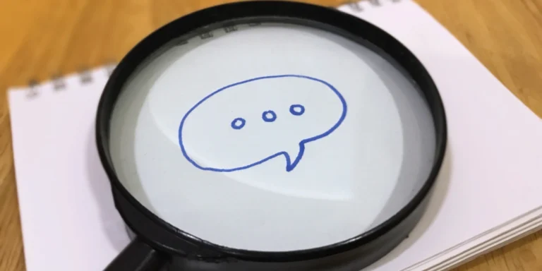 Magnifying glass over a notebook page, highlighting a blue speech bubble with three dots