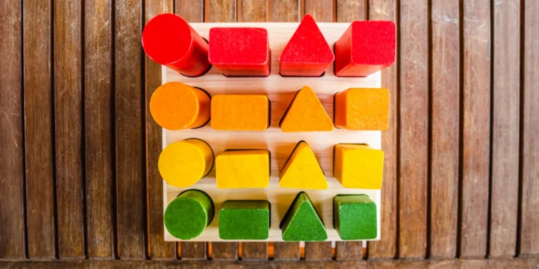 Colorful wooden counting toy with four rows of shapes (circles, squares, triangles) in red, orange, yellow, and green on a wooden grid.